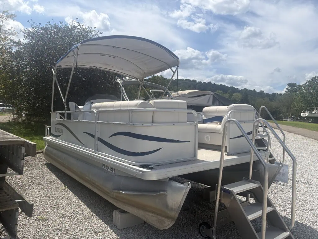 White pontoon boat with canopy on gravel lot