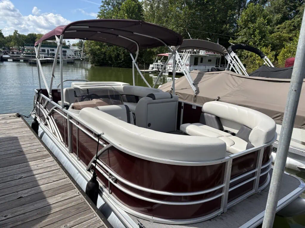 Maroon pontoon boat docked at a tree-lined marina