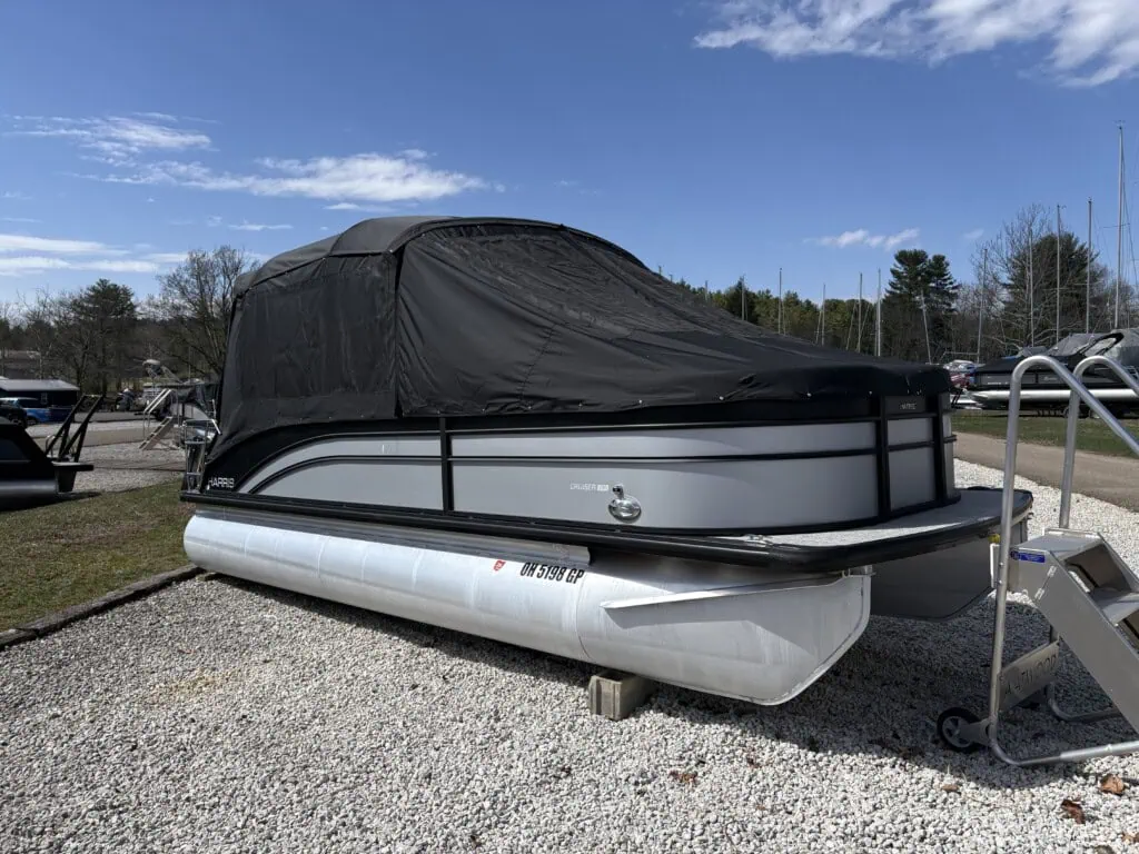 Covered pontoon boat parked on gravel lot.