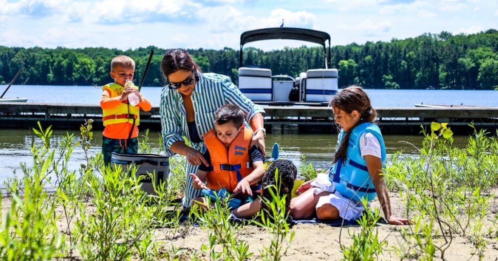 Family enjoying the beach at Atwood Lake with a pontoon boat in the background