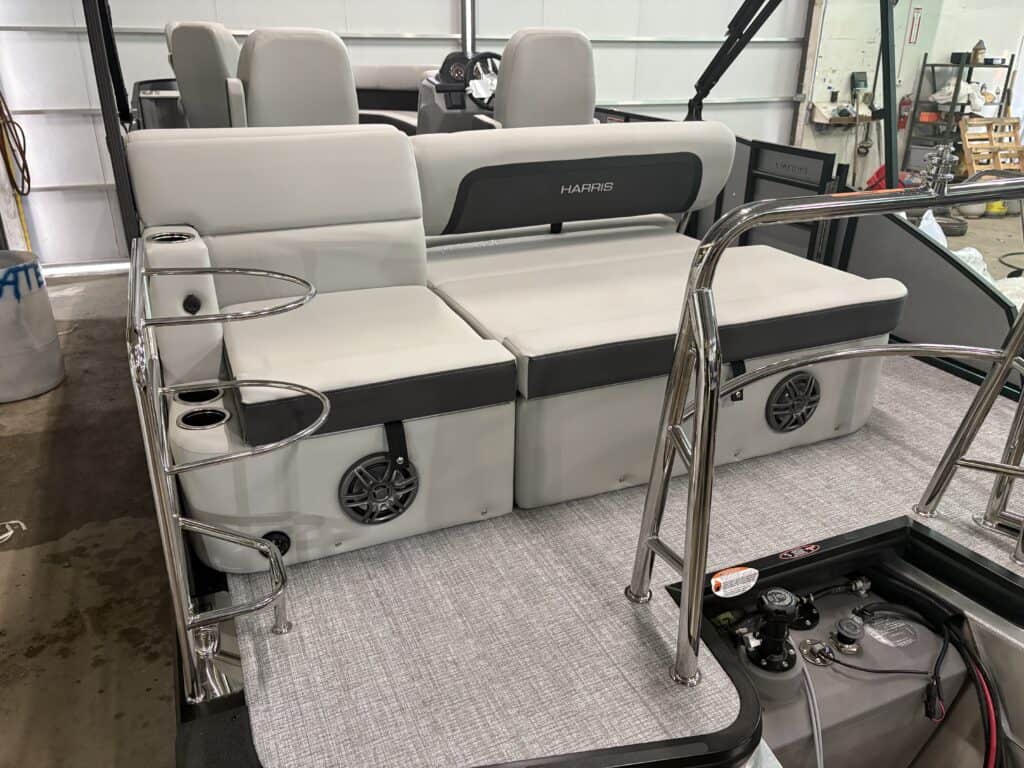 The interior of the 2025 Harris Cruiser 230 showcases gray seating and speakers, with sleek metal railings and convenient cup holders. The light-colored carpeting complements this SLDH model's modern elegance perfectly.