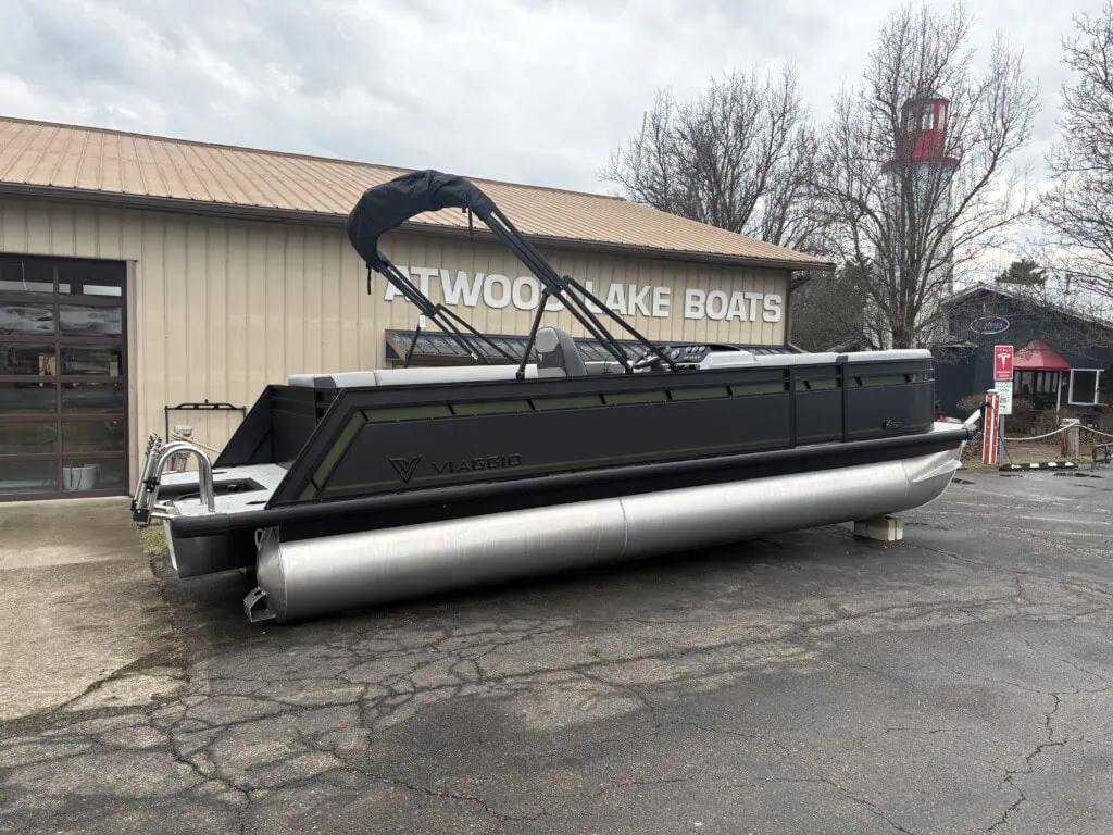 Black pontoon boat outside boat dealership.